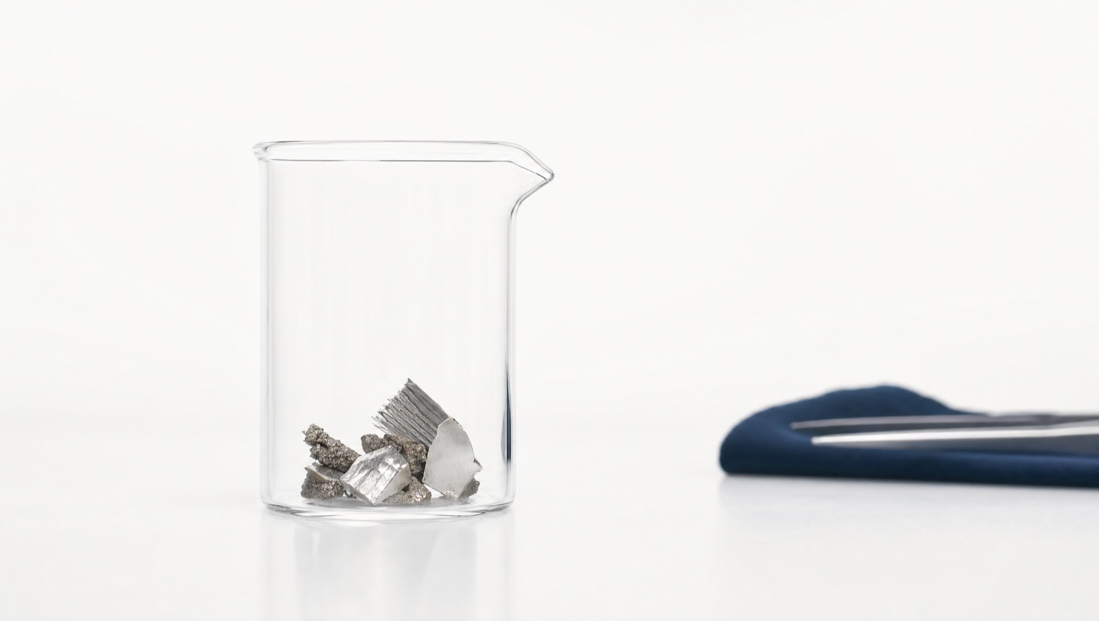 Recovered metal fragments in a laboratory beaker on a white bench