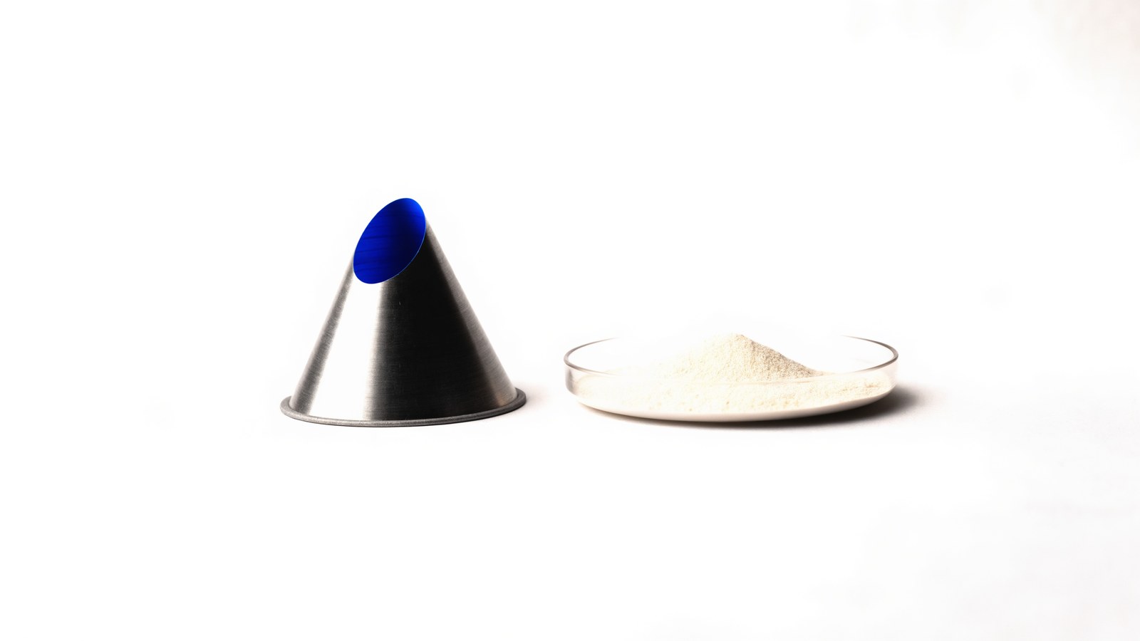 A machined cone with a blue inner face beside a dish of fine powder